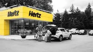 Yellow rental office building with white vehicles parked outside and a car being loaded onto a transport truck