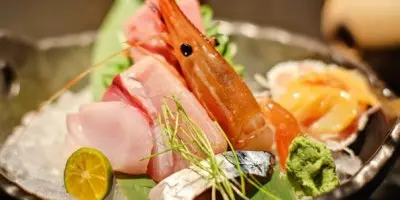 Assorted raw fish and shrimp arranged on ice with citrus slices and garnish on a green leaf platter