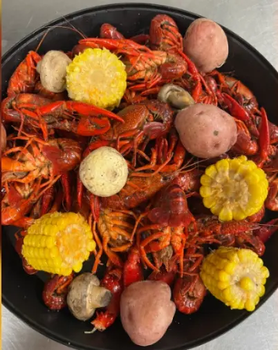 Cooked crawfish with corn, potatoes, and onions arranged on a black plate