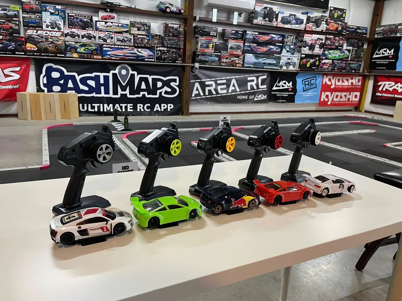 Collection of remote-controlled toy cars and controllers displayed on a table in an indoor RC racing facility