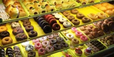 Assorted donuts and pastries with glazes and toppings displayed in yellow boxes behind glass counter