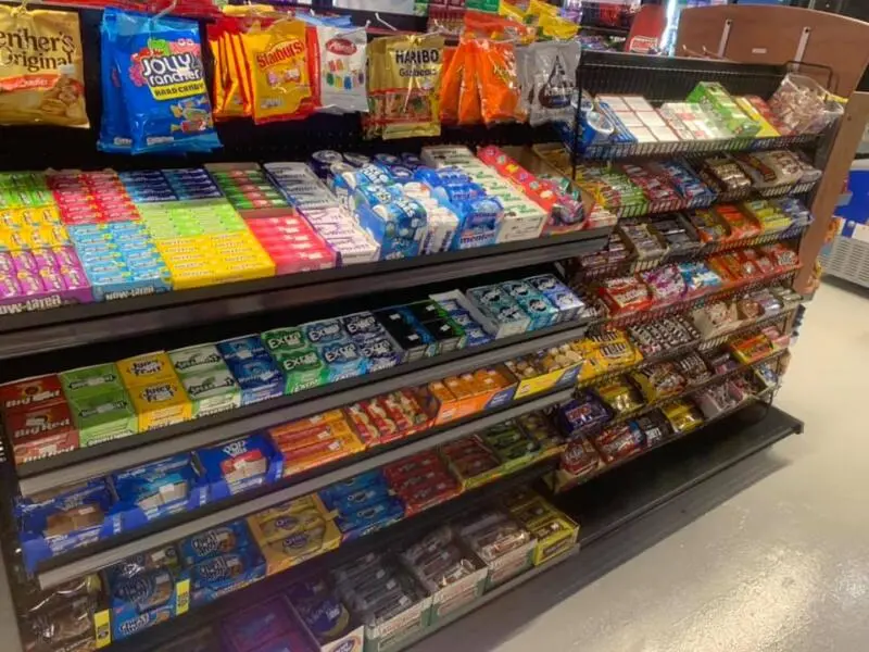 Stocked shelves of colorful packaged snacks, candy, and beverages in a convenience store display