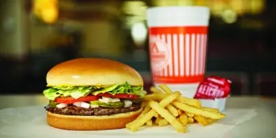 Burger with lettuce and tomato, French fries, and soft drink with red and white cup on counter