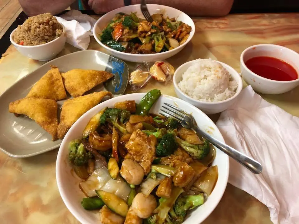 Assorted Chinese dishes including stir-fried chicken with vegetables, fried wontons, rice, and sauce on white plates