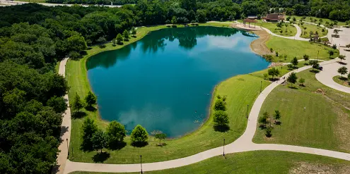 Aerial view of a large blue lake surrounded by green lawns, walking paths, and dense trees