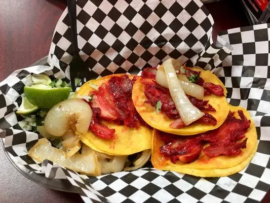Soft corn tortillas topped with sliced red meat, served with grilled onions and lime wedge on checkered paper