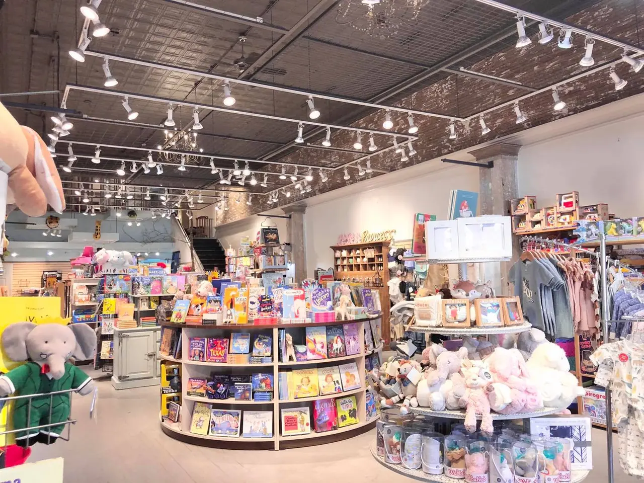 Bright retail store interior with circular display tables of toys, plush animals, and gifts, track lighting overhead, colorful merchandise throughout