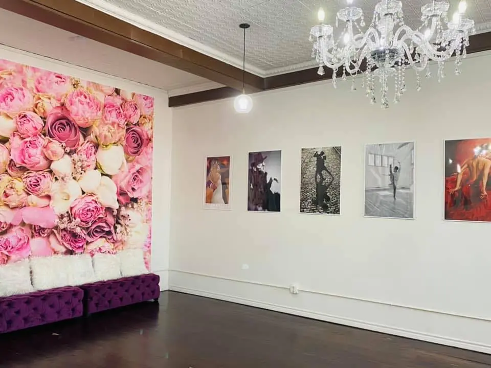 Spacious dance studio with large pink floral wall installation, purple velvet seating, crystal chandelier, and framed photographs on white walls