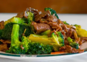 Beef and broccoli stir-fry on white plate with brown background