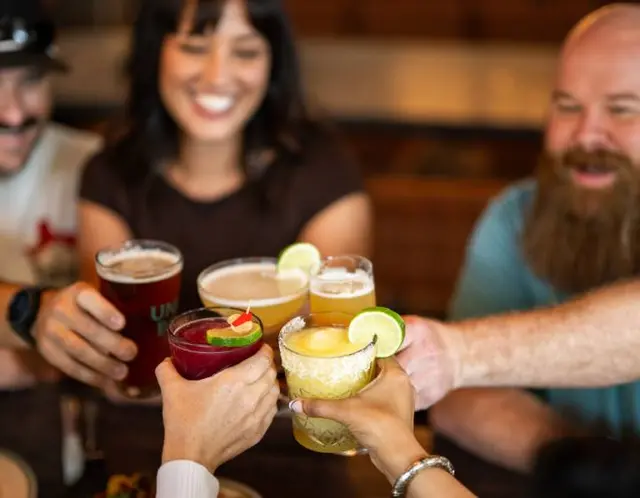 Three friends clinking glasses at a McKinney restaurant