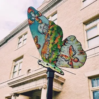 A steel Monarch butterfly sculpture painted with a McKinney streetscape and smaller butterflies, mounted outside the McKinney Performing Arts Center
