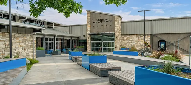 The entrance of Old Settler's Recreation Center, with glass doors, planter boxes and benches