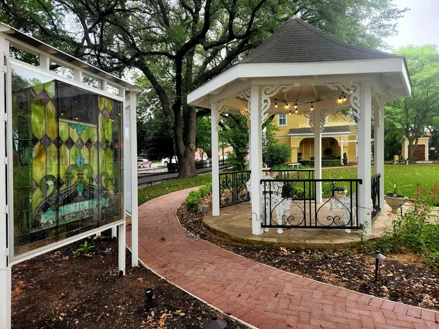 A stained-glass panel and the white gazebo along the brick path through the Heard-Craig gardens