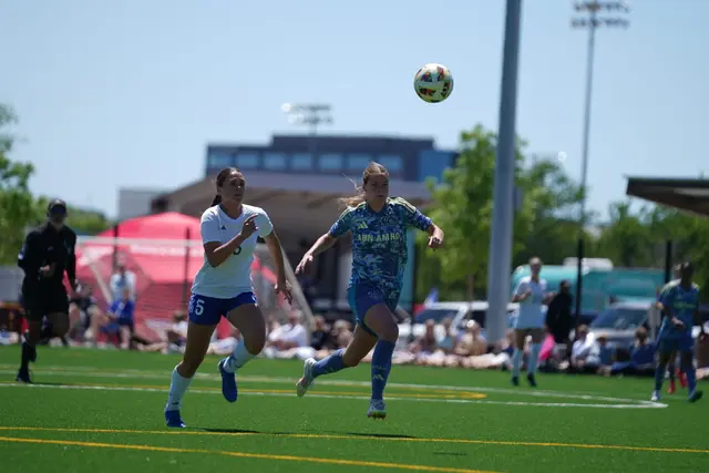 Two players chasing a soccer ball on a turf field at the International Girls Cup