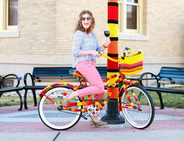 A woman on a bike holding a glass of wine at Arts in Bloom