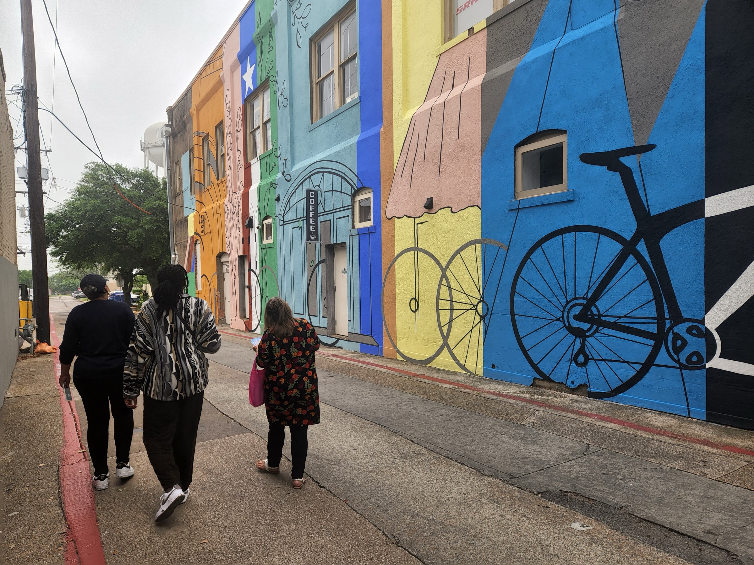 Three people walking past the painted bicycle mural in downtown McKinney